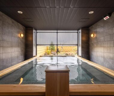 Wood-framed indoor onsen with tiled walls and garden view at 奥州平泉温泉旅館 itsumu in Iwate, Tōhoku