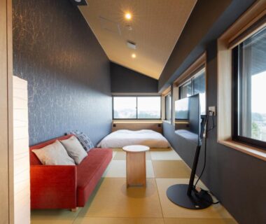 Tatami interior with low bed, red sofa, wooden table and large windows at 奥州平泉温泉旅館 itsumu, Iwate