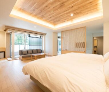 Modern guestroom with large bed, sofa, wood ceiling and balcony overlooking greenery at Yunomori Okunikko Yumoto Onsen in Tochigi