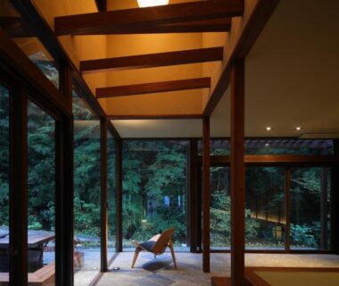 Floor-to-ceiling windows, wooden beams and lounge chair facing forest at Okuyugawara YUI in Kanagawa Japan