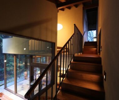 Interior wooden stairs and glass wall overlooking greenery at Okuyugawara YUI, Kanagawa, Japan