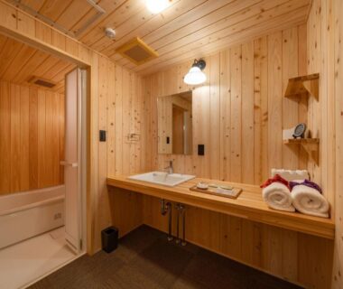 Wood-paneled bathroom with sink, mirror and towels at Wabi Sabi ryokan in Himeji, Hyōgo