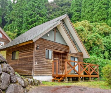 Wooden chalet with verandah and deck amid forested hillside near stone retaining wall