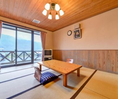 Bright tatami room with low wooden table, cushion, sliding glass doors and balcony view at Yasuragi no Sato Yamakuni, Ōita