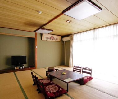 Tatami room with low table, zabuton cushions, floor chairs and shoji-style window at Awa Resort in Chiba