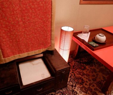 Red lacquer low table with tea set next to lamp and wooden chest in a Kyoto ryokan room
