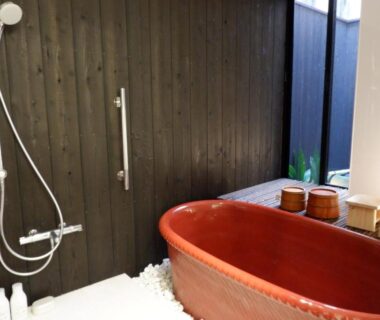 Indoor bathroom with red ceramic tub, shower fixtures and wooden buckets at Sawashoku auberge de Miyagawachō, Kyoto