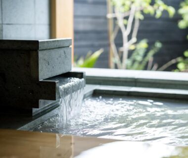 Flowing onsen water into a stone and wooden bath with garden view at Shukubō Shingetsu, Saga