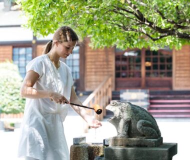 Woman ladling water from frog stone basin at Temple Hotel Kannonin in Gunma
