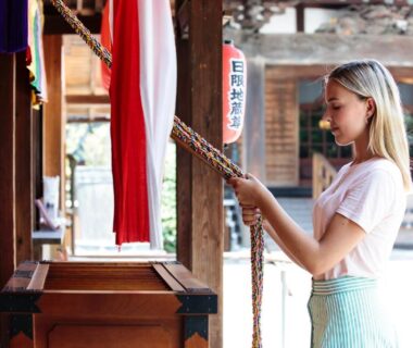 Visitor pulling temple bell rope at Kannonin temple grounds with wooden shrine details in Gunma