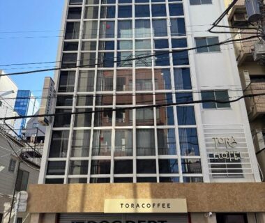 Tall modern building with grid glass facade housing TORA HOTEL Okachimachi in Tokyo city neighborhood