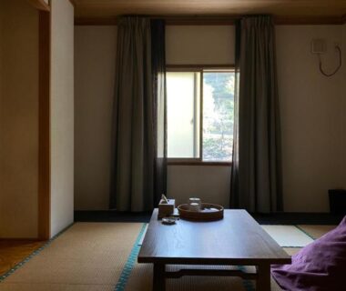 Traditional tatami room with low wooden table, floor cushions and window view at Hôtel Kumoi in Sōunkyō, Hokkaidō