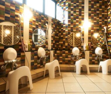 Mosaic-tiled onsen wash stations with stools and handheld showers at Hôtel Kumoi, Sōunkyō Onsen, Hokkaidō Japan
