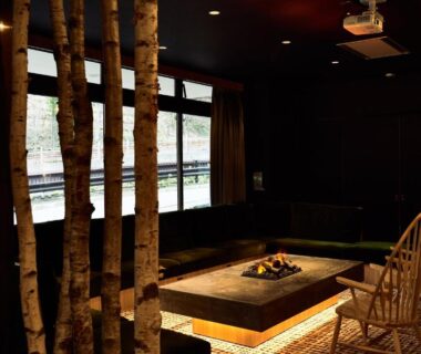 Low-lit lounge with birch trunks, wooden chairs and sunken hearth at Hôtel Kumoi Sōunkyō Onsen Hokkaidō