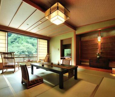 Tatami room with low table, floor chairs, shoji screens and large window overlooking greenery at Yama no Chaya, Kanagawa