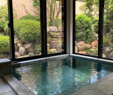 Indoor stone onsen bath with windows overlooking a rock garden at Yamashiroya Resort, Nagano, Chūbu