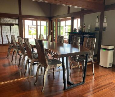Long wooden dining table with metal chairs and shoji screens overlooking greenery