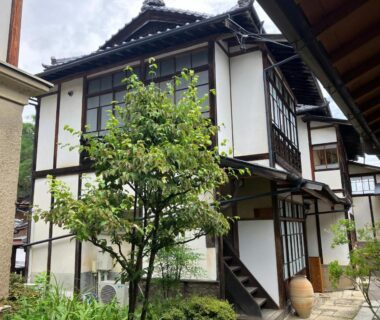 Two-story traditional ryokan building with wooden beams and small courtyard tree in Nagano