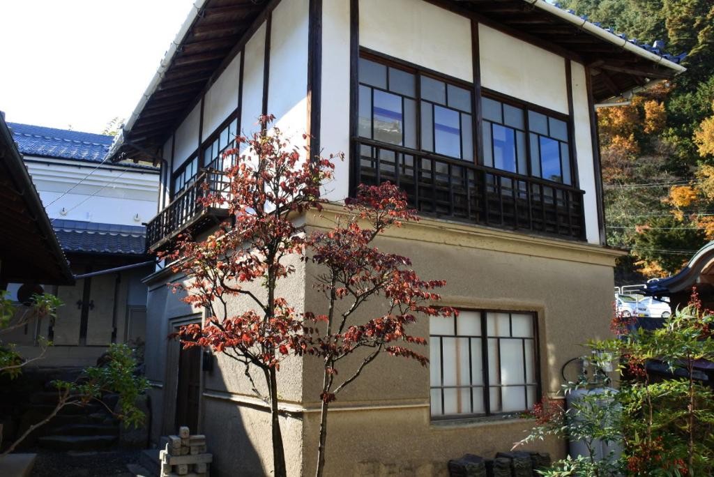 Traditional ryokan exterior Yamashiroya Resort Nagano Two-story traditional Japanese ryokan exterior with wooden framed windows and a small red-leaved tree at Yamashiroya Resort Nagano