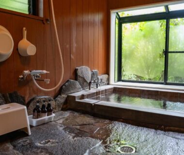 Indoor stone bathing area with wooden paneling and window view at Syaranoki in Oita, Kyushu