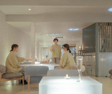 Guests in light robes conversing in a softly lit modern ryokan lounge at 巛-sen-Yugawara, Kanagawa