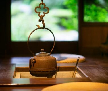 Cast iron kettle suspended above a sunken irori hearth, wooden interior and verdant garden view at Wadaya, Ishikawa
