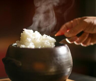 Hand serving steaming rice from earthen pot at Wadaya ryokan in Ishikawa