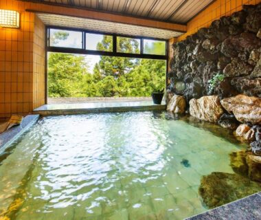 Stone-walled indoor onsen bath with large window overlooking lush garden at Wadaya, Ishikawa