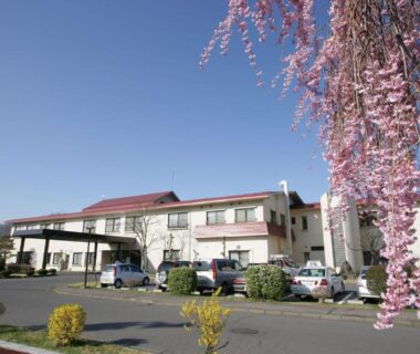 Exterior view of Nunobiki Onsen Komoro with cherry blossoms and parked cars in Nagano