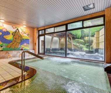 Indoor onsen bath with decorative wall mural and glass doors to outdoor bathing area at Shikibu no Yakata Izutsuya Fukushima