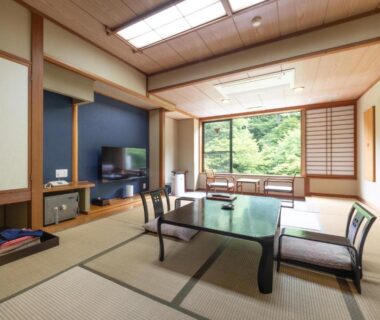 Tatami room with low table, zaisu chairs, shoji screens and large window overlooking greenery at Shikibu no Yakata Izutsuya