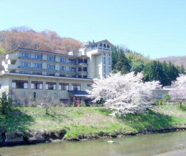 Riverside multi-story ryokan Shikibu no Yakata Izutsuya with cherry blossoms by a river in Fukushima Tohoku