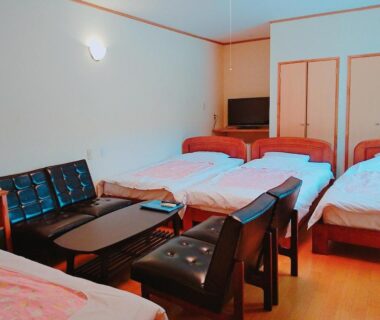 Multi-bed ryokan room with wooden floor, low seating area, TV and three single beds in Shizuoka