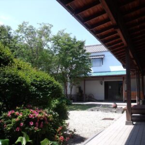 Wooden engawa veranda overlooking gravel courtyard with shrubs and entrance at Oyado Shinshima Shizuoka