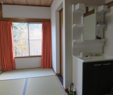 Tatami room with sink vanity, window with orange curtains and compact entry at Oyado Shinshima, Shizuoka