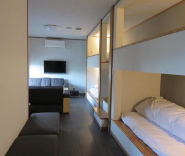 Recessed bed alcove with bedding, lounge sofa and TV in a minimalist room at Oyado Shinshima, Shizuoka