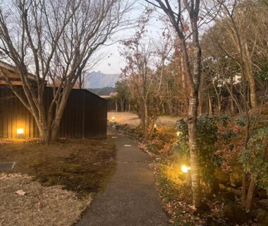 Lantern lit garden path between wooden Oyado Daikonya buildings with bare trees and distant mountain in Kumamoto Kyushu