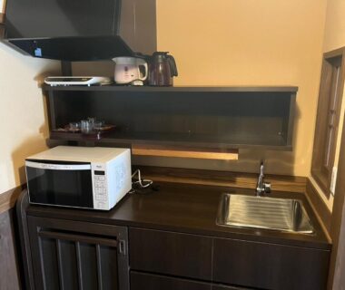 Small kitchenette with microwave, kettle, stainless sink and wooden cabinetry at Oyado Daikonya, Kumamoto, Kyushu