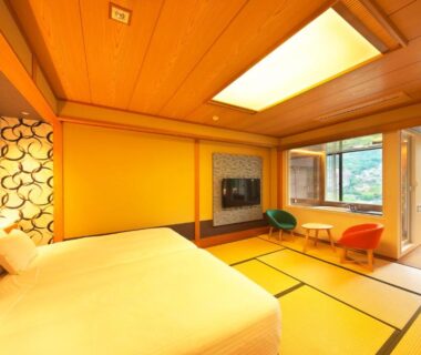 Tatami room with Western bed, low table, two chairs and greenery visible through large window at Oyado Zuiyō
