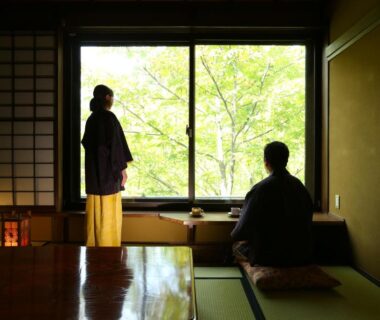 Two guests in tatami room with shoji screens and large window overlooking green trees at Keikoku no Yu Nagano