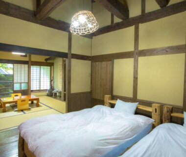 Room with two Western beds, tatami seating area, shoji screens and exposed timber beams at Ōgi Onsen, Kumamoto