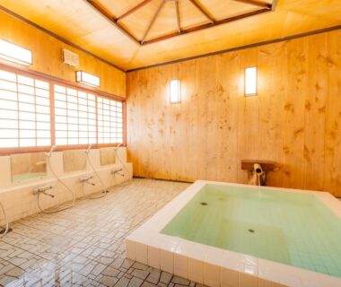 Wood-paneled communal bathing room with square soaking tub and shower stations at Ryokan Isobe Kyoto