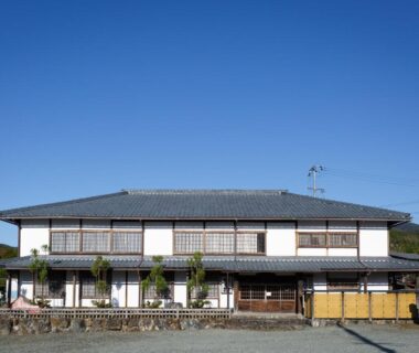Two-story ryokan with tiled roof, shoji windows and wooden veranda under clear blue sky in Kyoto