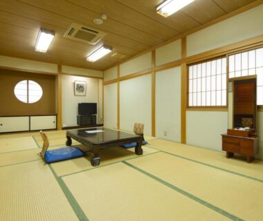 Spacious tatami room with low table, floor cushions, shoji screens and TV in a traditional ryokan setting