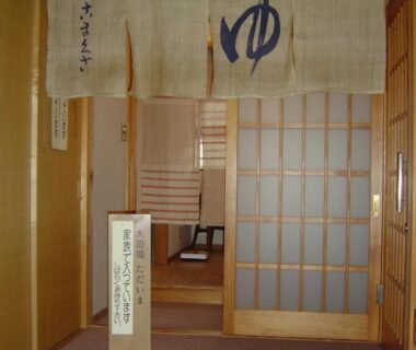 Woven noren with yu symbol above entrance to indoor onsen area, shoji doors and wooden corridor