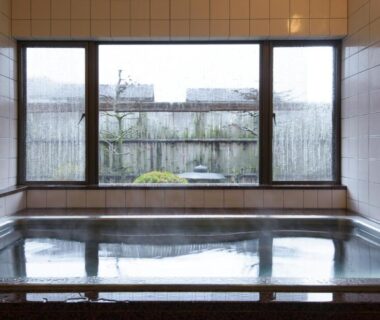 Tiled indoor bath with wooden trim and large window overlooking a small garden at Ryokan gastronomique Komakusa, Gifu, Chūbu