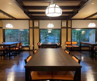 Dining room with dark wooden tables, cushioned chairs, large framed windows and hanging lanterns at Ryoan Kawaki Nagano