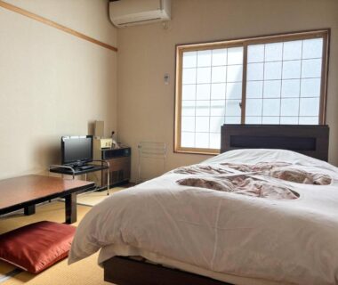 Tatami-floored room with Western bed, low table, shoji window and compact TV at 旅館FURUYA in Nagano