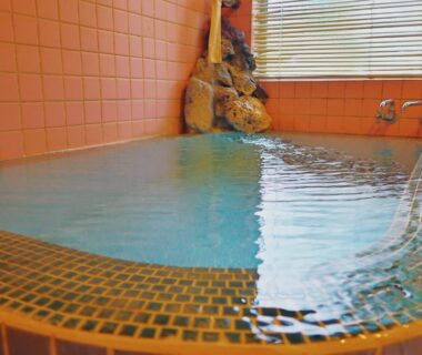 Indoor orange tiled onsen bath with mosaic edge and bamboo blind at 旅館FURUYA in Nagano