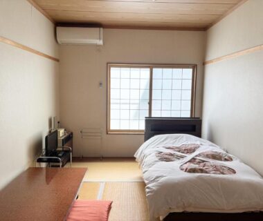 Tatami flooring with futon bedding, low table, shoji window and compact TV in simple ryokan room